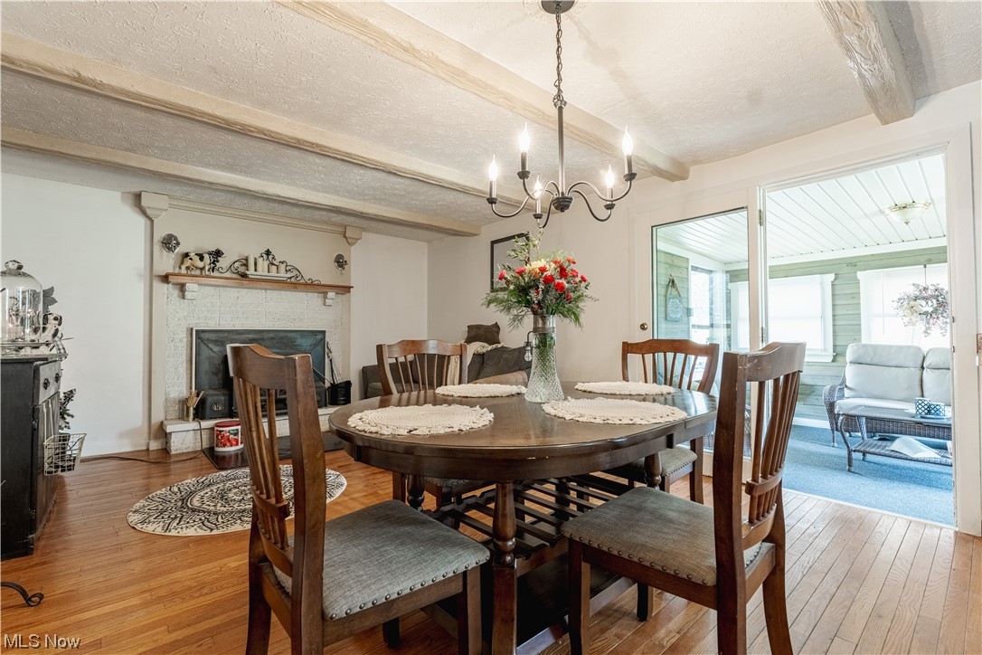 10450 Gavers Road Hanoverton, OH 44423 - Photo 14 of 50 Dining space with light hardwood / wood-style floors, a textured ceiling, a fireplace, beamed ceiling, and a chandelier