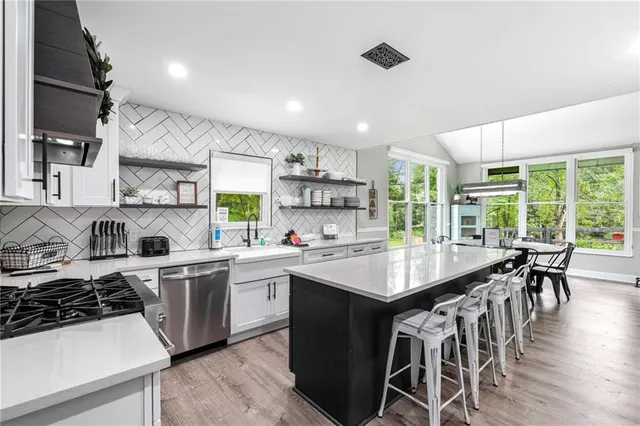 a kitchen with stainless steel appliances a refrigerator a stove a dining table and chairs with wooden floor