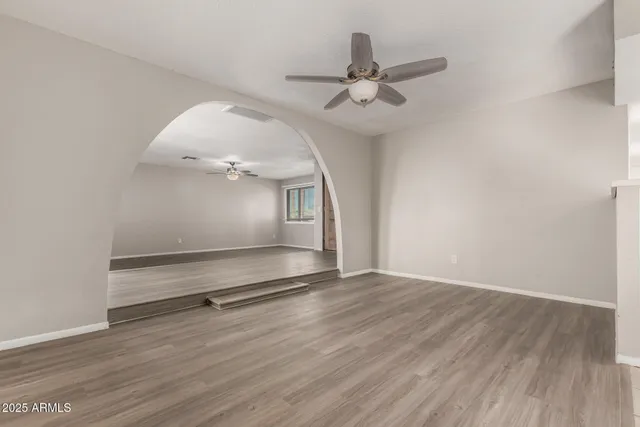 an empty room with wooden floor fan and windows