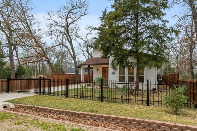 a view of a white house in a big yard with large trees and plants