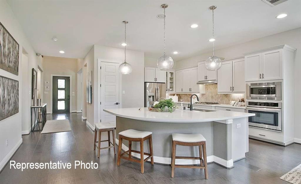 2845 Taylor Trail Corinth, TX 76210 - Photo 2 of 14 Contemporary kitchen featuring a curved island with seating, white shaker cabinetry, stainless steel appliances, and a tile backsplash