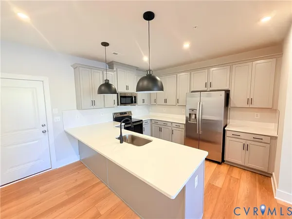a large kitchen with kitchen island a stove a sink a refrigerator and white cabinets with wooden floor