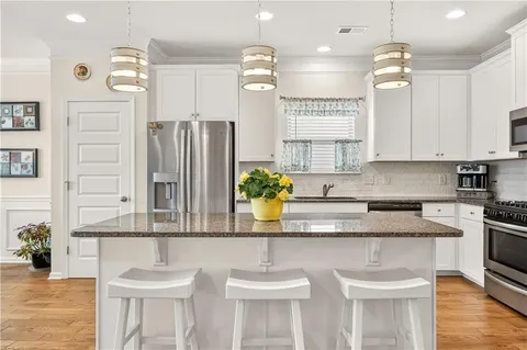a kitchen with kitchen island granite countertop stainless steel appliances a sink a stove a refrigerator cabinets and wooden floor