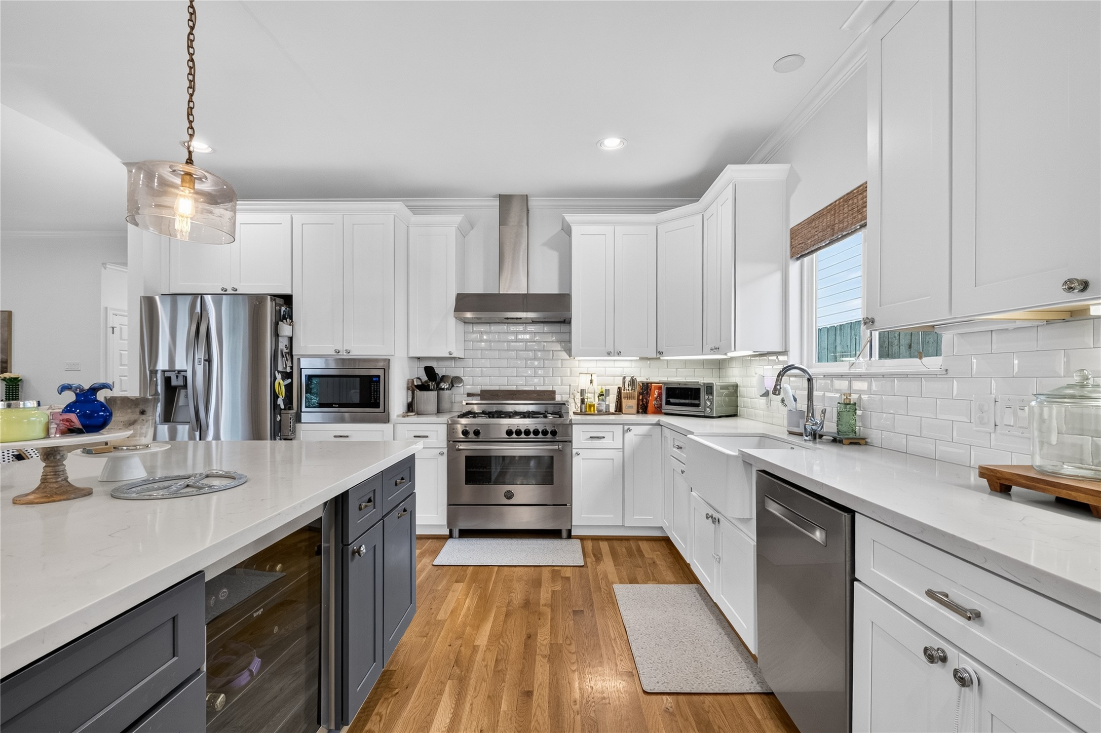 1722 Chippendale Road Houston, TX 77018 - Photo 10 of 41 Modern kitchen featuring sleek stainless steel appliances, elegant white cabinetry, and a spacious island with pendant lighting, all set on warm hardwood floors.
