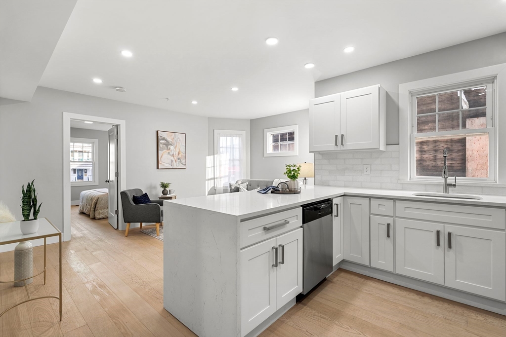 679-683 Columbia Road, Unit 1 Boston, MA 02125 - Photo 9 of 31 a kitchen with a sink dishwasher a stove and white cabinets with wooden floor