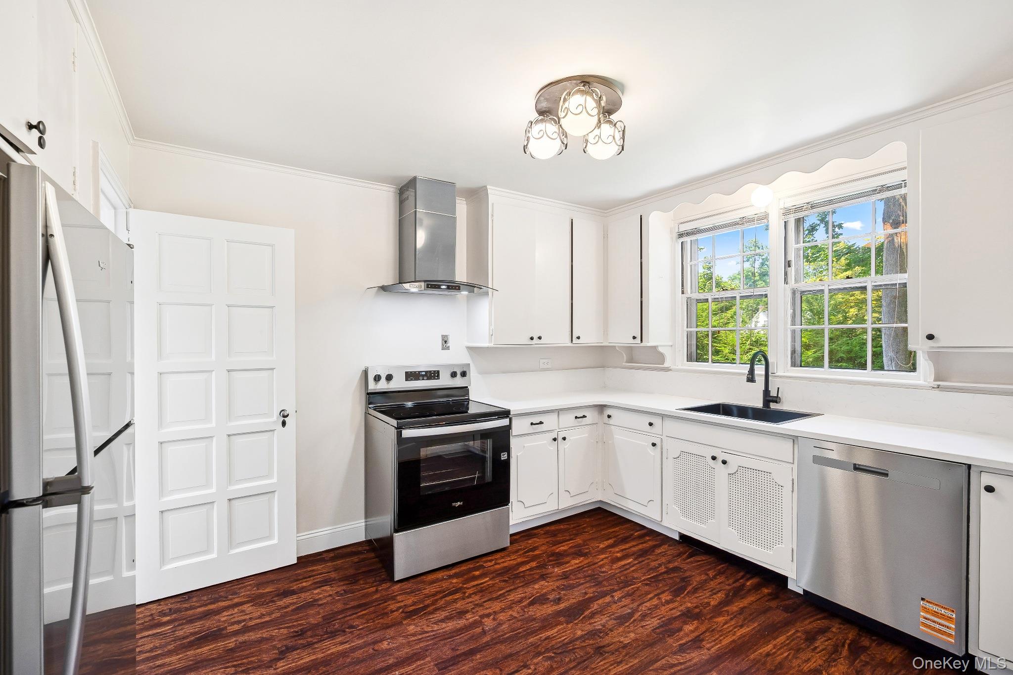 6 Fox Meadow Road Scarsdale, NY 10583 - Photo 4 of 20 Kitchen featuring appliances with stainless steel finishes, wall chimney range hood, dark wood-style flooring, ornamental molding, and light countertops