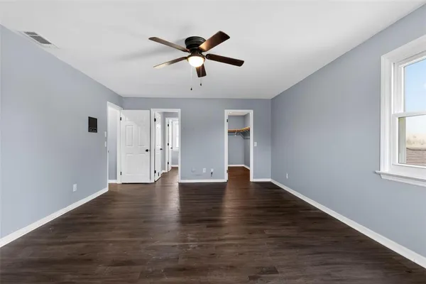 an empty room with wooden floor ceiling fan and windows