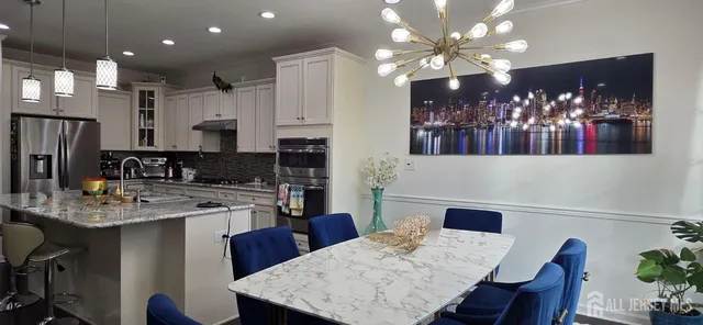 a kitchen with stainless steel appliances kitchen island granite countertop a dining table chairs and a refrigerator