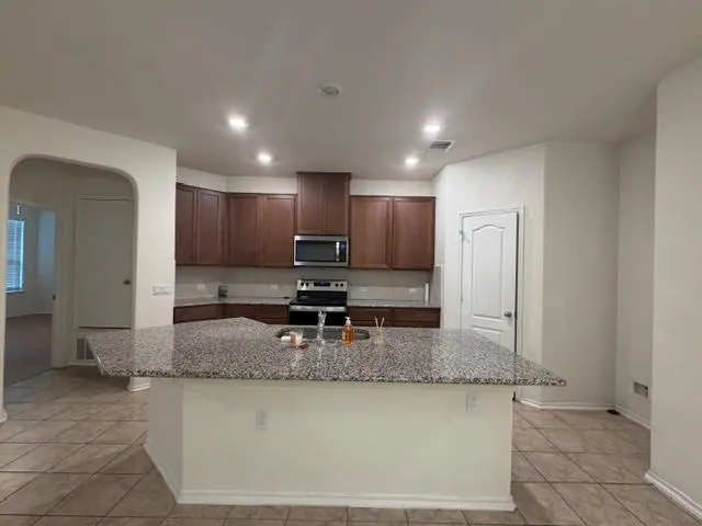 a view of a kitchen with kitchen island granite countertop a refrigerator and a stove top oven