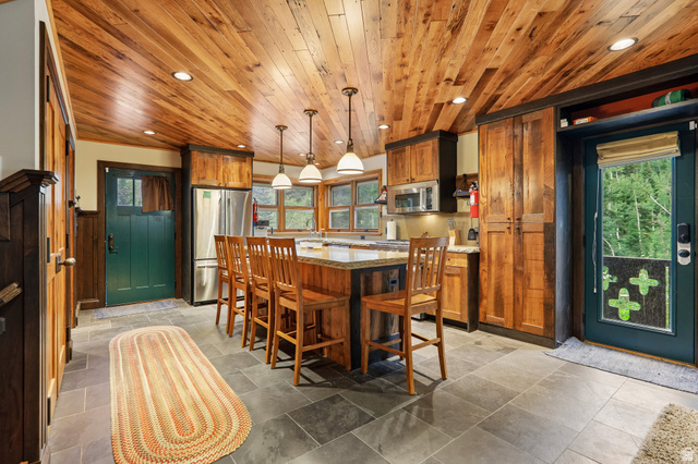 10205 East Moose Loop Road Salt Lake City, UT 84121 - Photo 10 of 50 Kitchen featuring a wood-panel ceiling with recessed lighting, central island with seating, stainless steel appliances, stone tile flooring, and rustic wood cabinetry