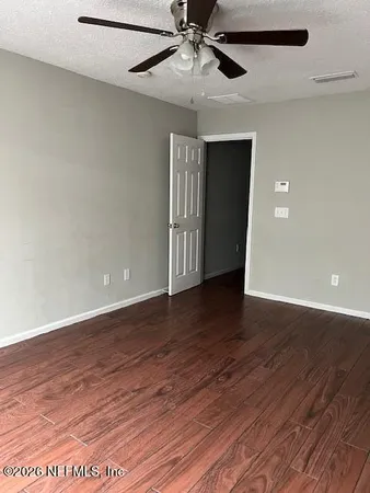 a view of an empty room with wooden floor and a ceiling fan