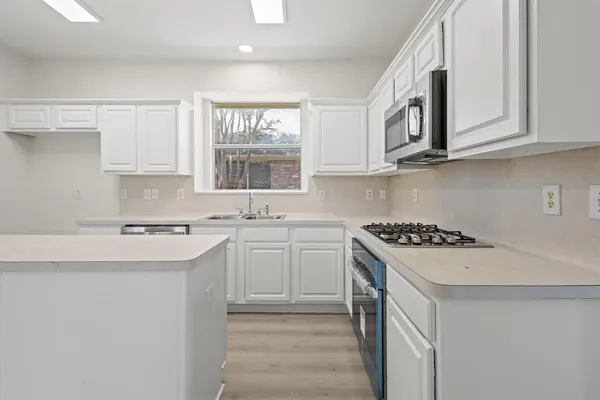 a kitchen with white cabinets appliances a sink and a window