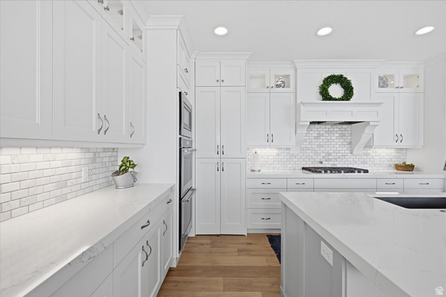21 Pier Place Tooele, UT 84074 - Photo 20 of 112 Bright kitchen featuring white shaker cabinetry, light countertops, subway tile backsplash, stainless steel double wall ovens, and wood-finish flooring