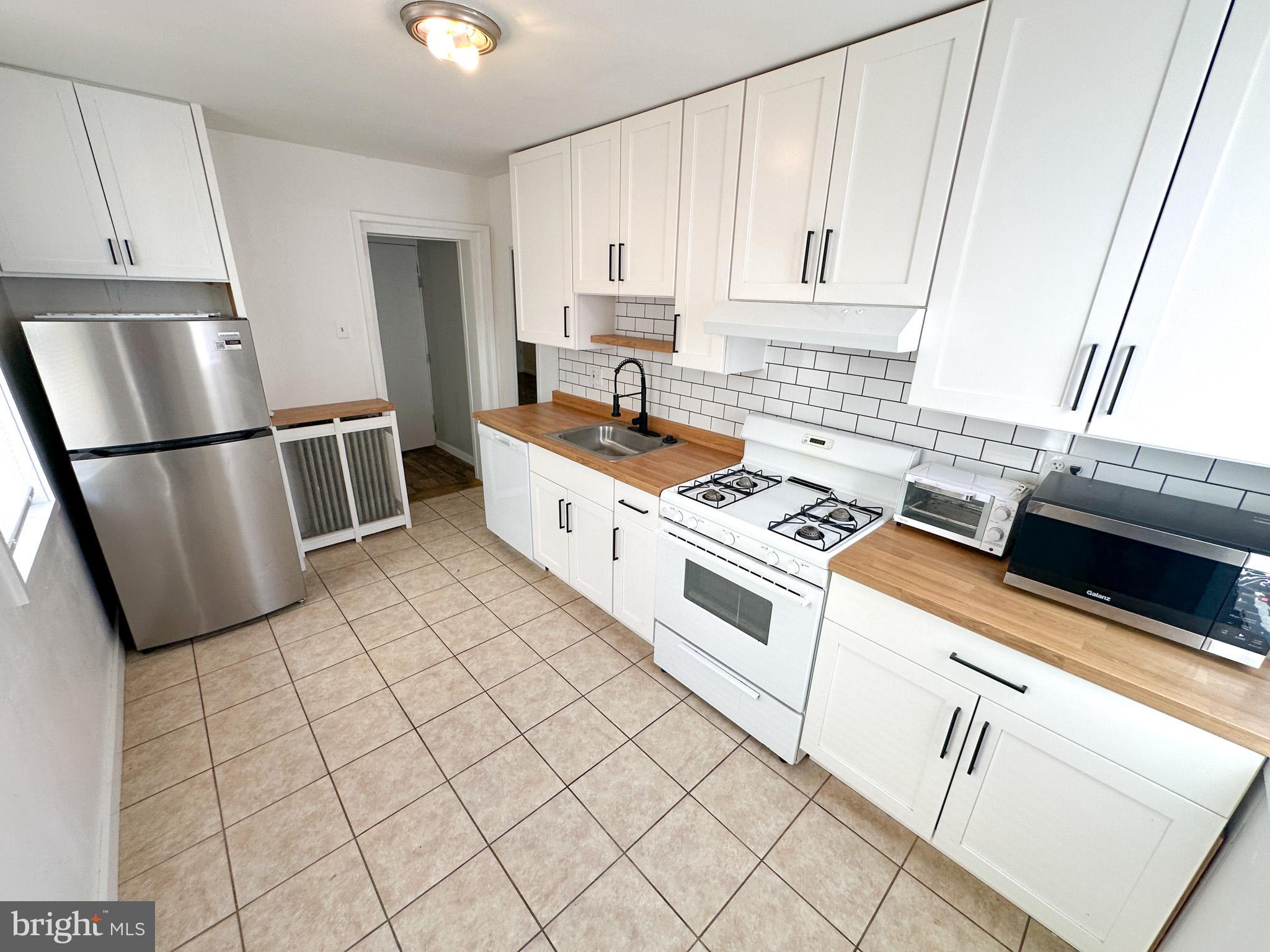 a kitchen with white cabinets a sink a stove a refrigerator and a window