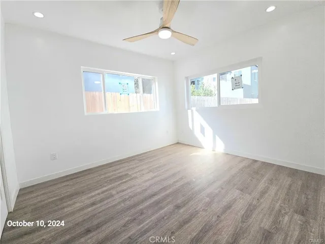 an empty room with wooden floor chandelier fan and windows