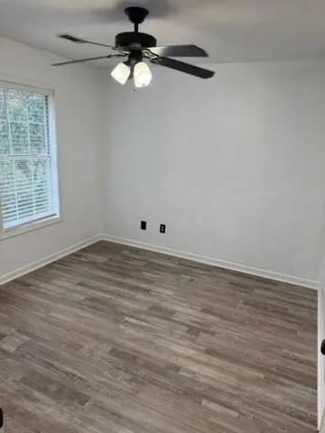 an empty room with wooden floor fan and windows
