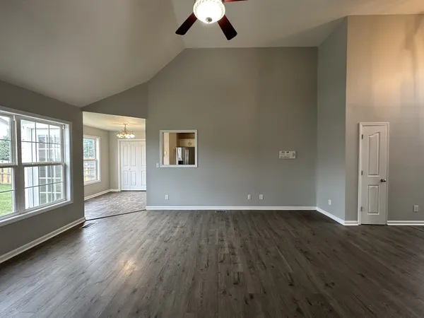 an empty room with wooden floor chandelier fan and windows