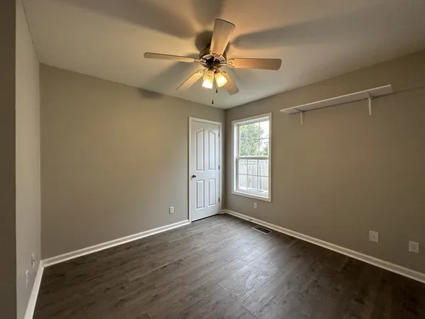 an empty room with wooden floor fan and windows