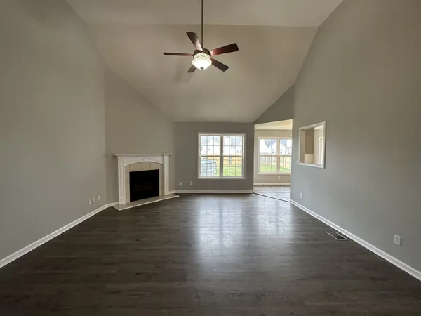 an empty room with wooden floor fireplace and windows