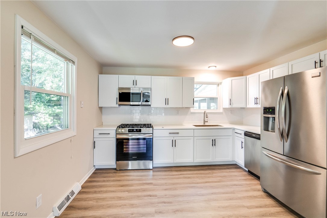 1173 Dussel Road Kent, OH 44240 - Photo 10 of 16 Kitchen with backsplash, light countertops, light hardwood floors, white cabinetry, and stainless steel appliances