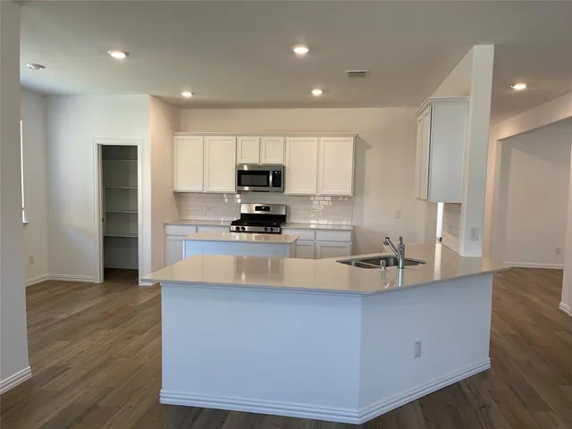 a large kitchen with kitchen island a stove a sink a refrigerator and white cabinets with wooden floor