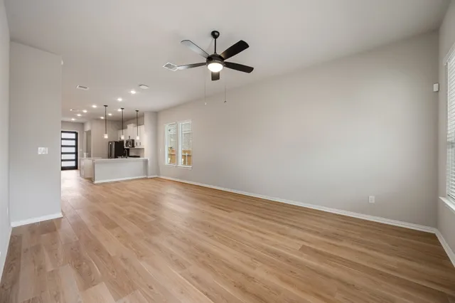 a view of an empty room with wooden floor and a ceiling fan