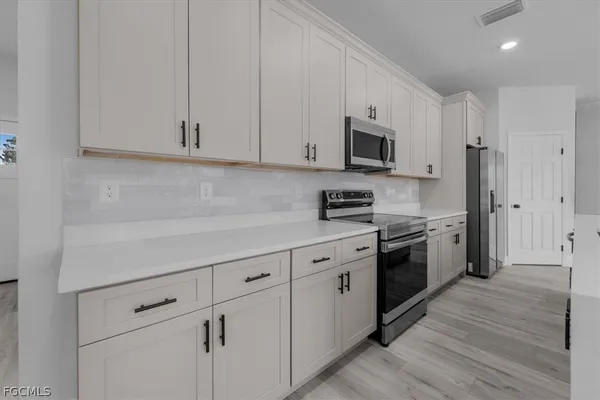 a kitchen with stainless steel appliances granite countertop white cabinets a sink a stove a refrigerator and a microwave