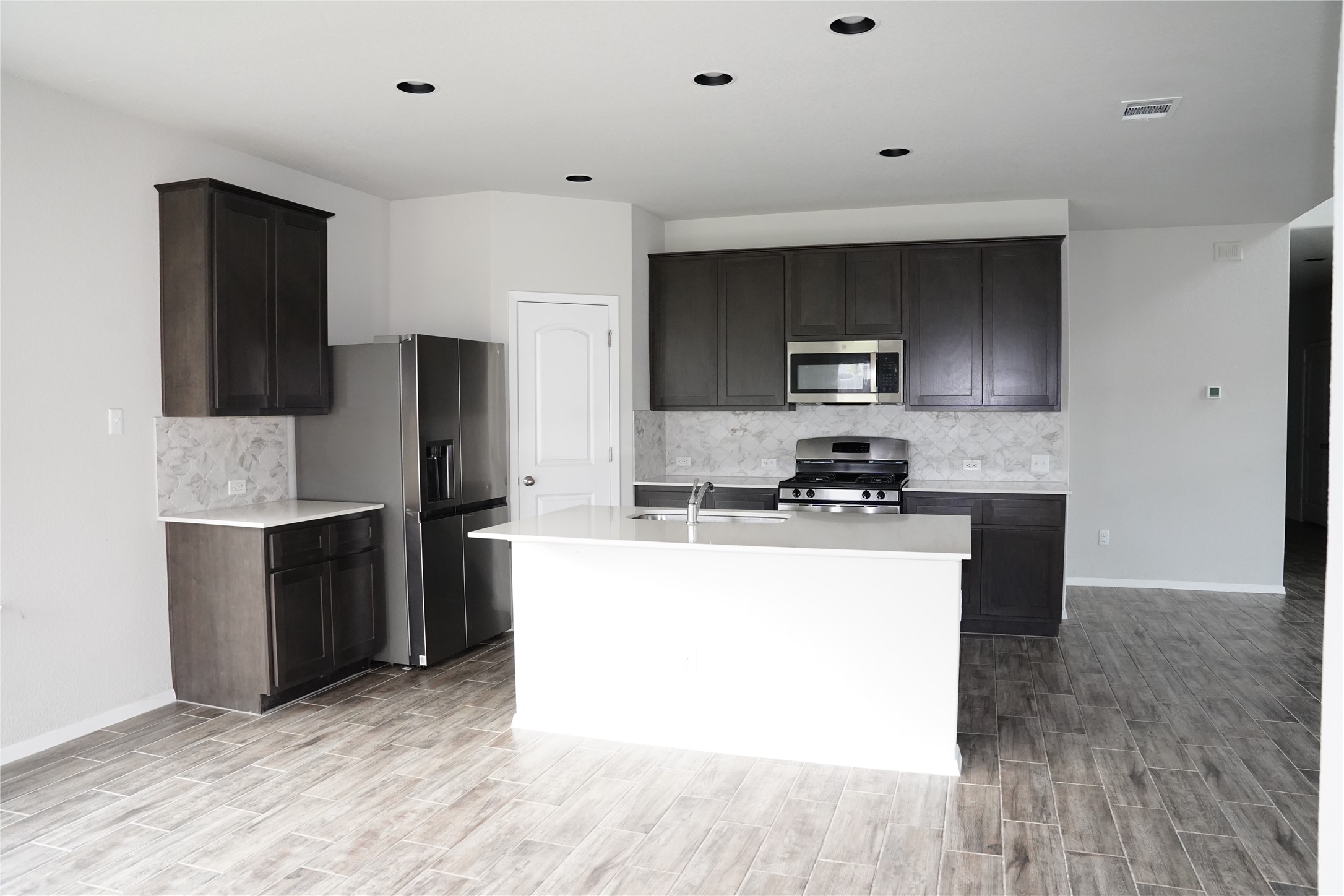 117 Crescent Street Georgetown, TX 78626 - Photo 7 of 38 A well-lit kitchen with dark cabinetry, modern stainless steel appliances, and a central island with a sink.