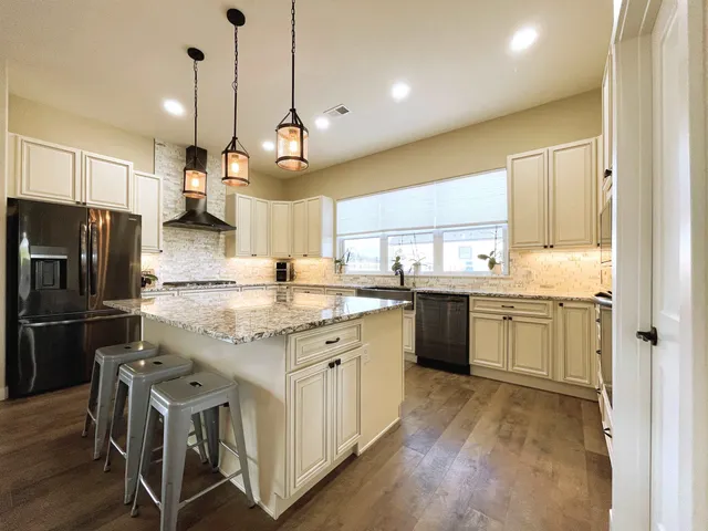 a kitchen with stainless steel appliances granite countertop a refrigerator a sink dishwasher a oven and a dining table with wooden floor