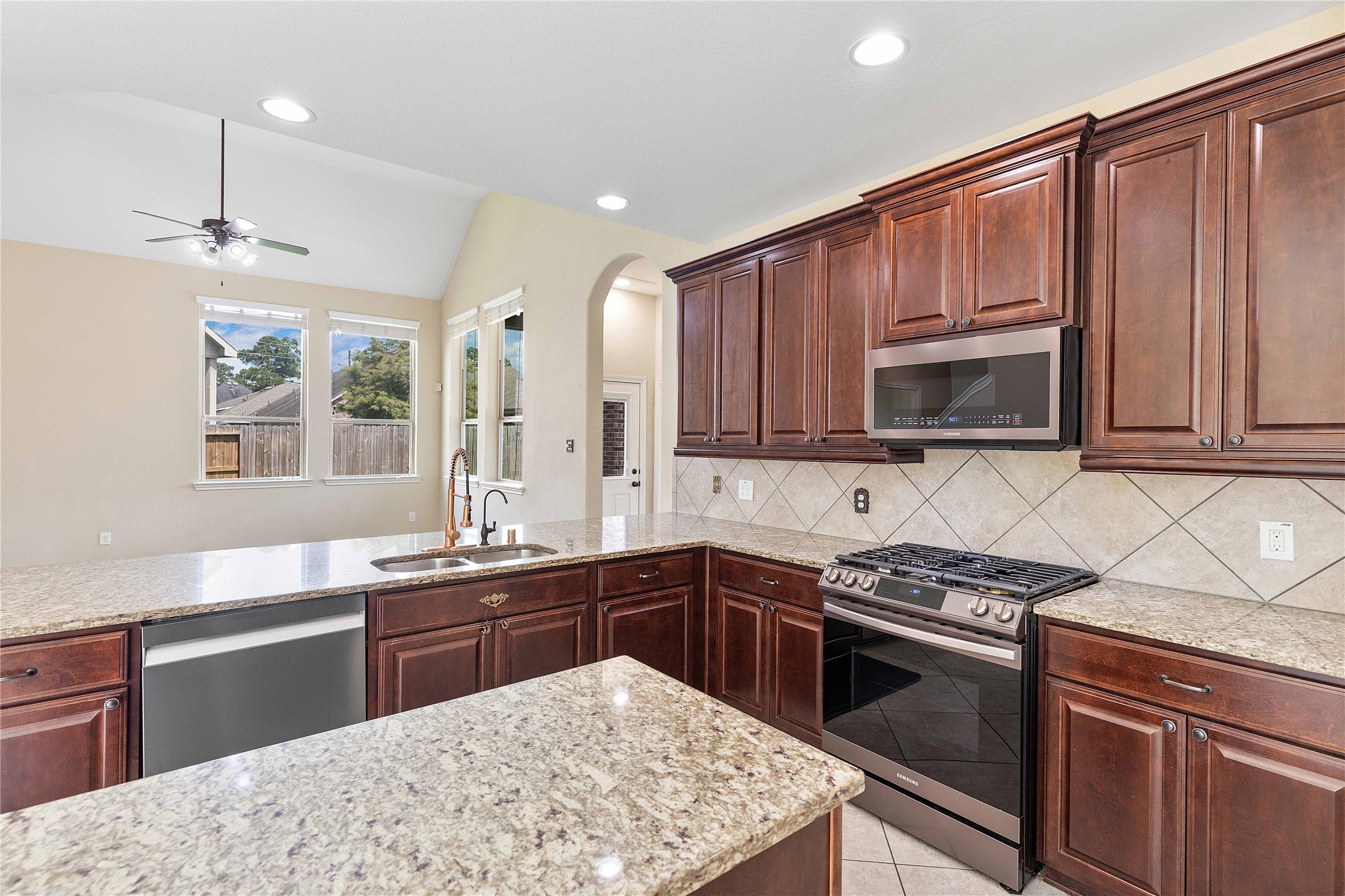 17206 Upper Ridge Lane Humble, TX 77346 - Photo 5 of 50 This kitchen features elegant dark wood cabinets, granite countertops, and stainless steel appliances. It has an open layout with large windows for natural light, a ceiling fan, and a view into the living area, creating a welcoming and functional space.
