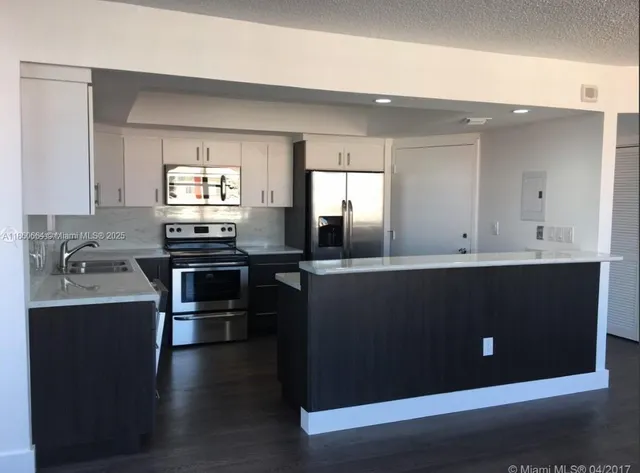 a kitchen with stainless steel appliances kitchen island granite countertop a refrigerator a sink and white cabinets