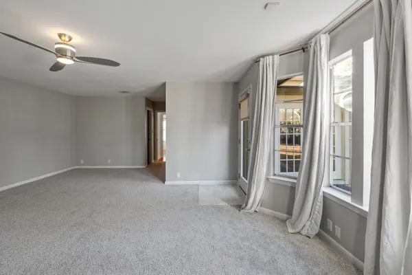 an empty room with chandelier fan and windows