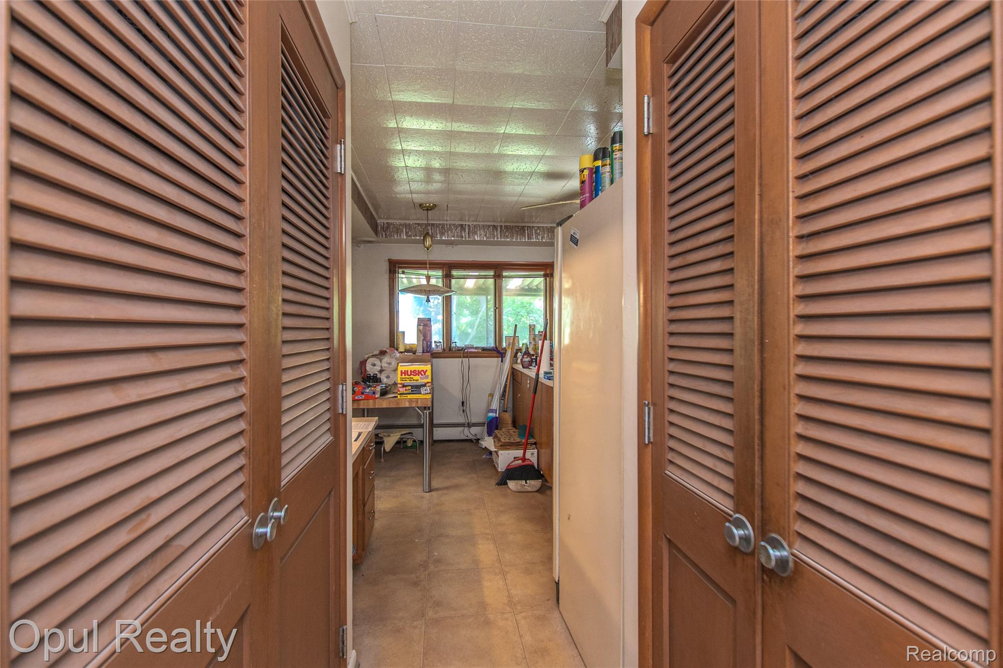 6455 Norham Road Bloomfield Hills, MI 48301 - Photo 32 of 93 Two louvered wood-finish doors framing a hallway, with a window visible at the far end and a built-in overhead light fixture