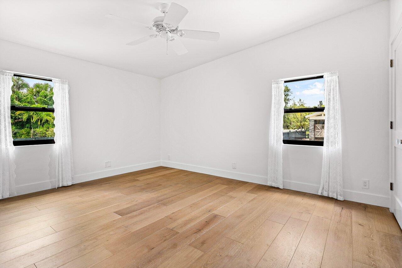 17270 Rocky Pines Road Jupiter, FL 33478 - Photo 53 of 69 an empty room with wooden floor chandelier fan and windows