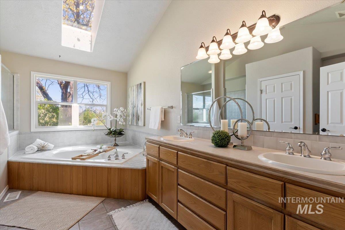 147 East Indian Crk Road Boise, ID 83716 - Photo 16 of 43 Bathroom featuring a built-in jetted tub with wood-panel surround, a skylight, and a dual vanity with light-colored countertops
