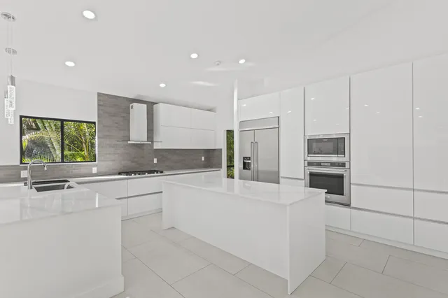 a large white kitchen with stainless steel appliances kitchen island granite countertop a refrigerator and a stove top oven