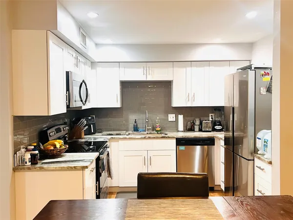 a kitchen with stainless steel appliances granite countertop a stove a sink dishwasher and white cabinets with wooden floor