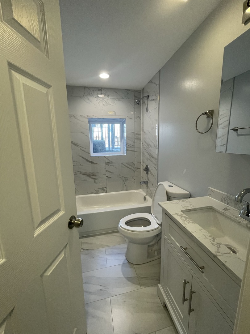 1024 West Ainslie Street, Unit 1 Chicago, IL 60640 - Photo 9 of 16 a bathroom with a granite countertop toilet a sink a mirror and bathtub