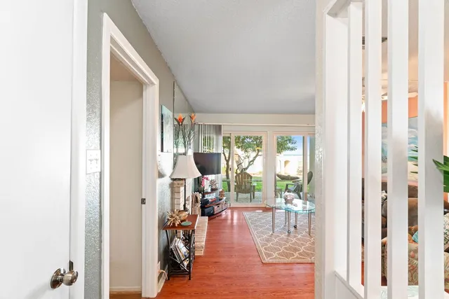 a view of a hallway to a livingroom with wooden floor and windows