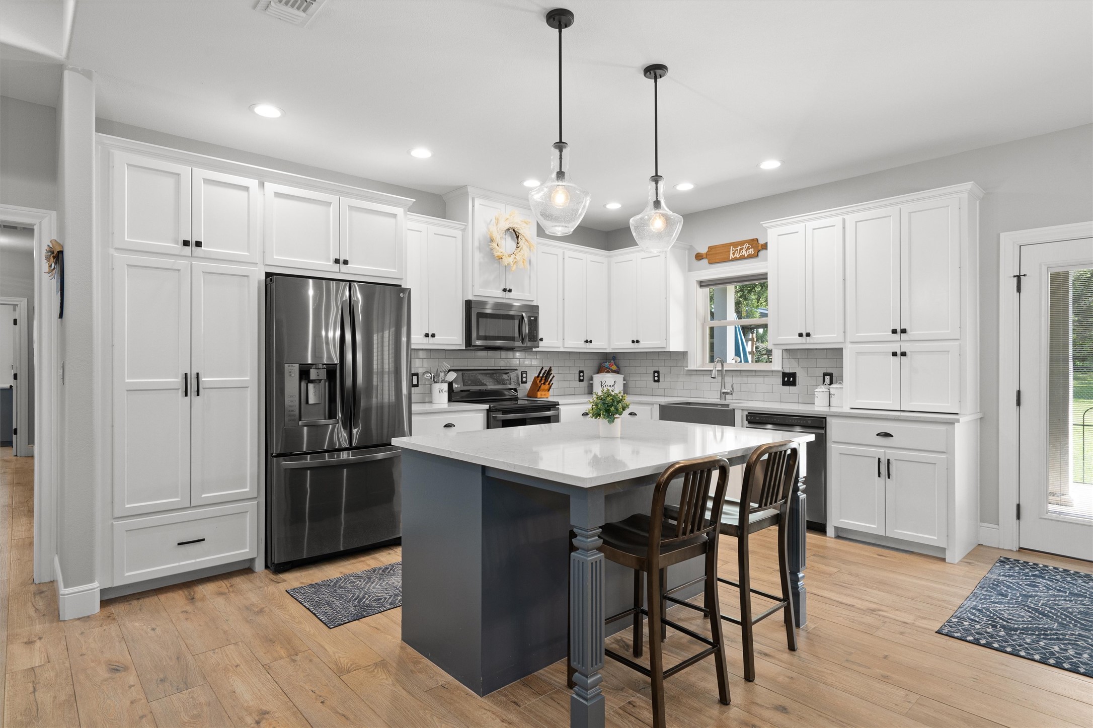 136 Fawn Hollow Elgin, TX 78621 - Photo 9 of 40 Spacious kitchen featuring white shaker cabinetry, stainless steel appliances, a central island with bar seating, pendant lighting, and wood-finish flooring