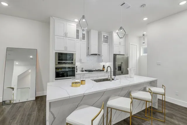 a kitchen with stainless steel appliances granite countertop a sink a stove a refrigerator and a dining table with wooden floor