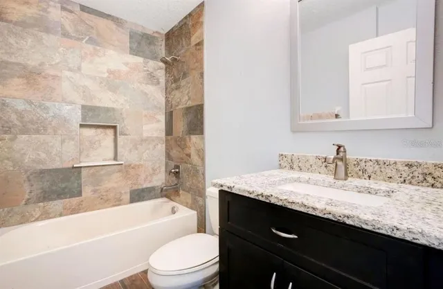 a bathroom with a granite countertop bathtub sink vanity mirror and toilet