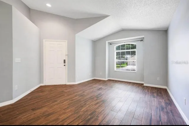 a view of an empty room with wooden floor and a window