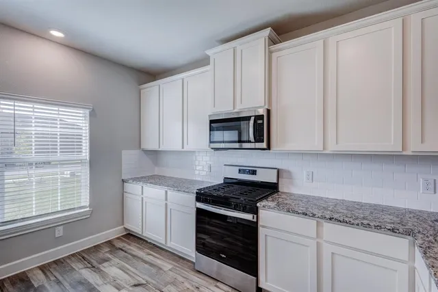 a kitchen with stainless steel appliances granite countertop white cabinets and a window
