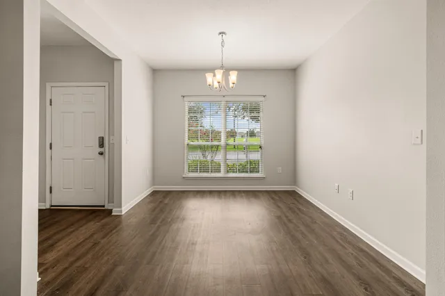 an empty room with wooden floor chandelier and windows