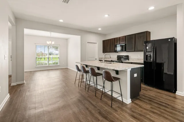 a kitchen with stainless steel appliances granite countertop a stove a refrigerator a sink a dining table and chairs