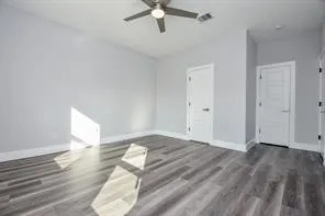 an empty room with wooden floor ceiling fan and windows