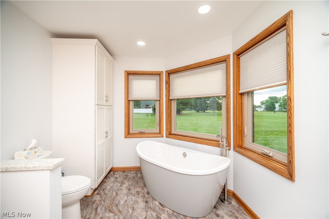 405 Airport Road Northwest Warren, OH 44481 - Photo 26 of 50 Freestanding soaking tub with a floor-mounted faucet, wood-finish window frames, recessed lighting, white built-in cabinetry, and wood-finish flooring