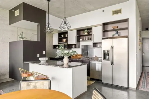 a kitchen with stainless steel appliances granite countertop a refrigerator a sink dishwasher a stove and a dining table with wooden floor