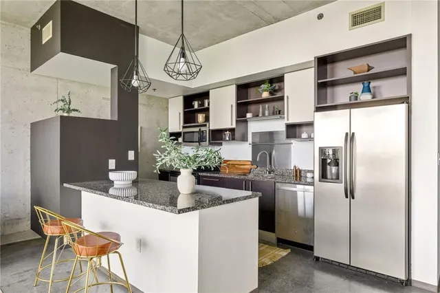 a kitchen with stainless steel appliances granite countertop a refrigerator a sink dishwasher a stove and a dining table with wooden floor